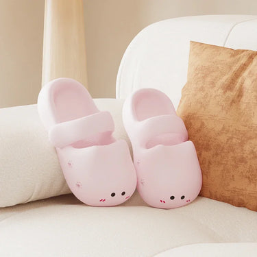 KittyNook Cat Co.'s Adorable Cat Face Comfort Sandals in pink with non-slip sole rest on a white sofa by a brown cushion.